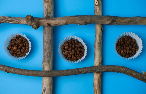 fragrant coffee beans are poured in a cupcake mold on a bright blue background, surrounded by natural textures of wooden sticks. for splash screens, labels, postcards, signs, announcement menus and more