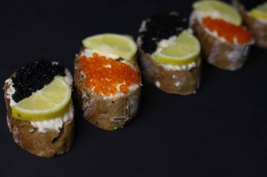 delicious healthy dark baguette bruschetta with melted cheese and red and black caviar and lemon for decoration on a black background. for screensavers labels advertising flyers banners postcards menus