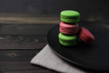 sweet bright tasty macaroon cakes of light green and pink color on a black plate and a wooden surface