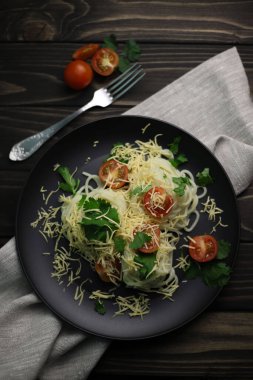 healthy hearty dinner of pasta with tomatoes, grated cheese and herbs on a wooden surface and in a black dish. for screensavers labels advertising flyers banners postcards menus