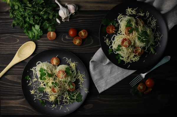 delicious fragrant pasta with grated cheese, red tomatoes, kenza greens and garlic on black plates and a wooden surface. for signboards splash screens labels banners menu flyers announcements