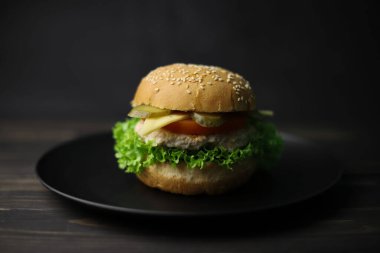 juicy delicious cheeseburger from bun with sesame meat patty cheese tomato and cucumber and green fresh lettuce and ketchup in red bottle on wooden dark surface