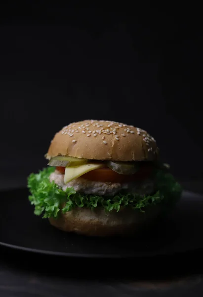 juicy delicious cheeseburger from bun with sesame meat patty cheese tomato and cucumber and green fresh lettuce and ketchup in red bottle on wooden dark surface