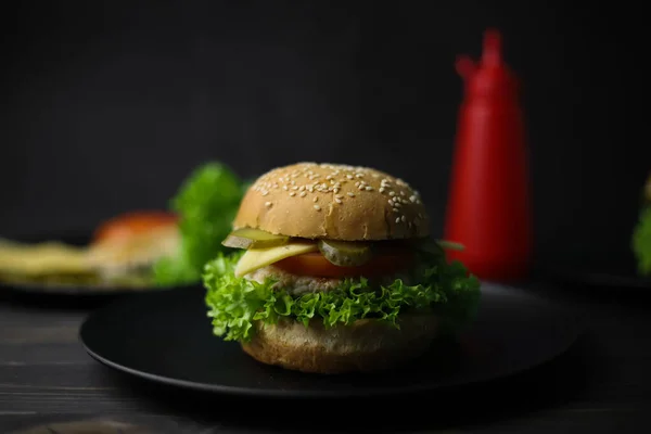 juicy delicious cheeseburger from bun with sesame meat patty cheese tomato and cucumber and green fresh lettuce and ketchup in red bottle on wooden dark surface