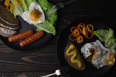 hearty healthy romantic breakfast of heart-shaped scrambled eggs and juicy sausages with green salad and fragrant bread in a black plate on a wooden surface