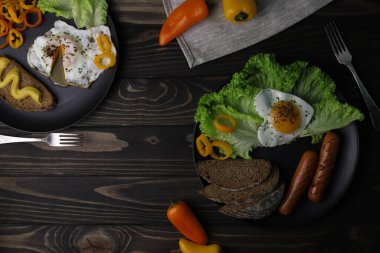 hearty healthy romantic breakfast of heart-shaped scrambled eggs and juicy sausages with green salad and fragrant bread in a black plate on a wooden surface