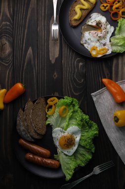 hearty healthy romantic breakfast of heart-shaped scrambled eggs and juicy sausages with green salad and fragrant bread in a black plate on a wooden surface