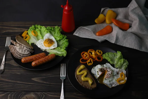 hearty healthy romantic breakfast of heart-shaped scrambled eggs and juicy sausages with green salad and fragrant bread in a black plate on a wooden surface
