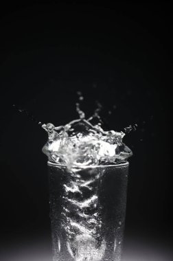 natural mineral clean healthy water in a transparent glass and drops of water splash out of it on a dark background. for banners labels splash screens postcards advertising signage