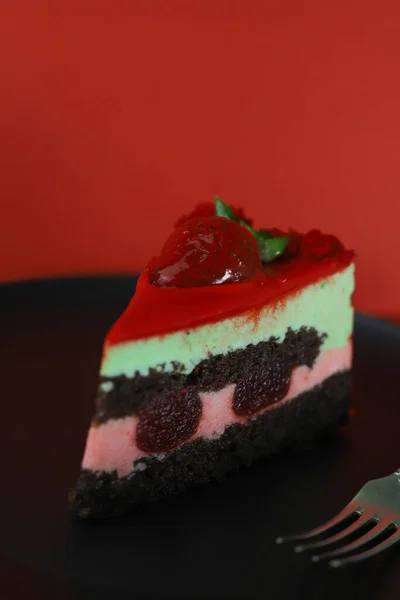 一片美味的甜而美丽的明亮的蛋糕 上面有草莓在一个黑色的厨房盘和一个红色的背景 周围装饰着粉红色的浆果 — 图库照片