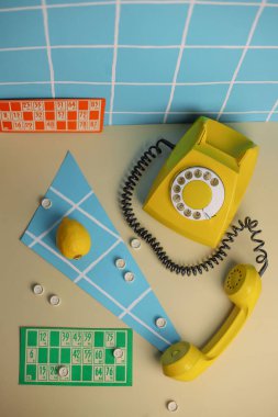 80 'lerin tarzında bir fotoğraf. Fotoğrafta parlak renkli bir retro telefon beyaz kareli bir duvarda mavi bir arka planda loto marmelat ve limon oyununun yanında.