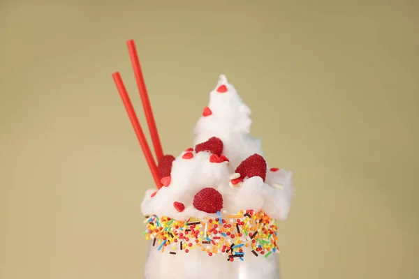 a cocktail of white cotton candy in a transparent glass decorated with red hearts and sprinkles of different colors with bright tubes and umbrellas cookies and raspberries