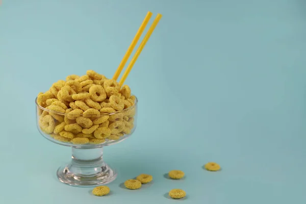 繊細なミントの背景に透明なガラスの黄色のリングの形で朝食のための健康的なコーンフレーク 広告ラベル用スプラッシュ画面看板チラシ広告 — ストック写真