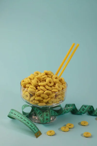 healthy corn flakes for breakfast in the form of yellow rings in a transparent glass on a delicate mint background. for advertising labels splash screens signs flyers advertising