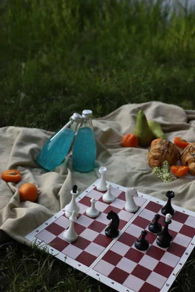 board logic game for family and friends picnic chess, the game is placed on a picnic blanket in nature and with croissants, apricot slices and drinks. for screensavers, postcards, advertising