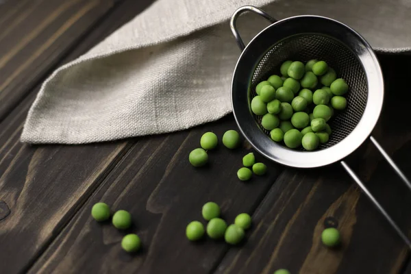 stock image young green peas in a tin mug and nearby lie peas and pods in a sieve on a dark wooden background. for screensavers, labels, postcards, flyers, etc.