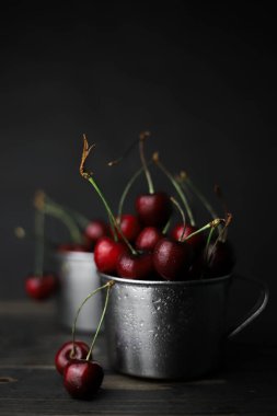 Beyaz dumanlı siyah bir arka planda siyah bir camda kırmızı-bordo renkli tatlı kirazlar. Kartpostallar, broşürler, afişler, etiketler, ekran koruyucular ve daha fazlası için