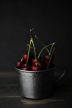 Beyaz dumanlı siyah bir arka planda siyah bir camda kırmızı-bordo renkli tatlı kirazlar. Kartpostallar, broşürler, afişler, etiketler, ekran koruyucular ve daha fazlası için