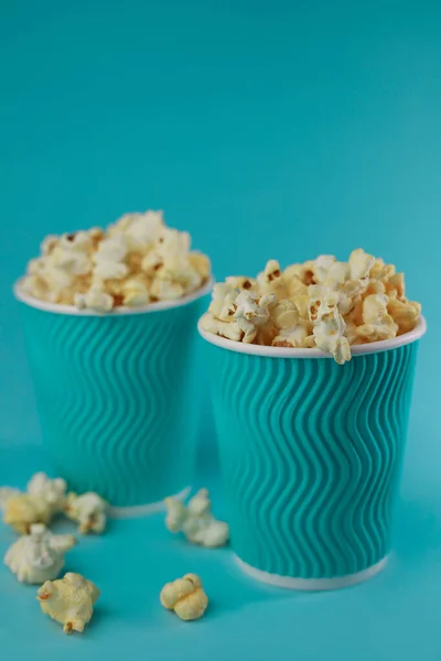 ready sweet and salty delicious popcorn is in a glass of bright aquamarine color on a light blue background. for postcards, screensavers, flyers, promo menus, etc.