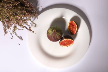 Kesik içinde taze incir beyaz bir tabakta yatıyor. Küçük çiçekli bir buketin yanında.