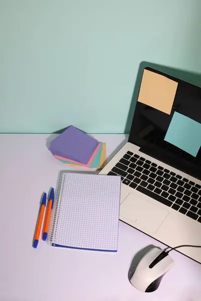 on a white background, a white laptop, a white computer mouse, a notepad, pens and multi-colored stickers for notes
