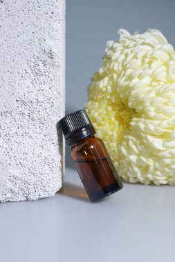 Şeffaf kahverengi bir şişe. Sıvı beyaz asterların yanında duruyor.