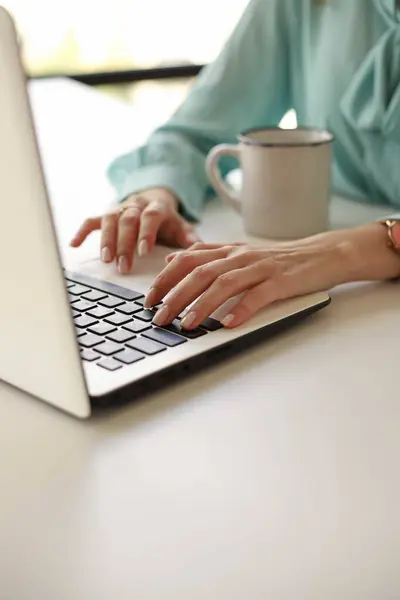 a girl in a blue blouse works at a table with a white laptop. business. cup next to her