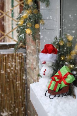 Noel Baba şapkalı bir kardan adam balkonda duruyor. Noel Baba 'nın kızağının yanında kırmızı kurdeleli yeşil ambalaj kağıdıyla hediyeler var. Etrafında ladin dalları var.