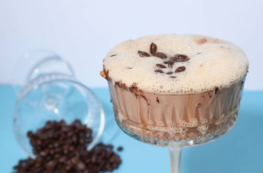 İç bakalım. Espresso Martini. Kahve çekirdekleri ile süslenmiş, beyaz-mavi arka planda bir bardakta kahve içilir.