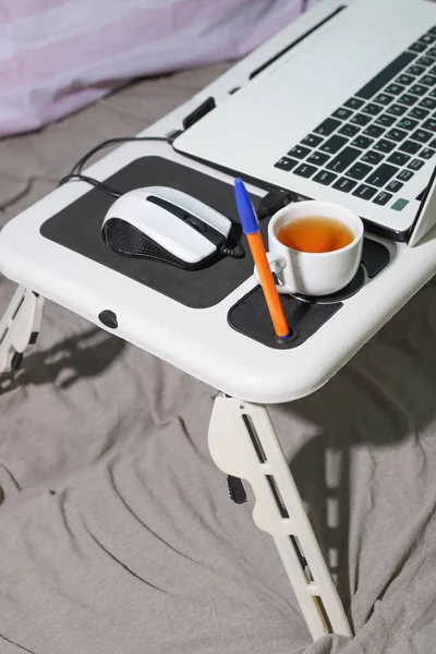 work at home in bed. For comfortable work, there is a transformable table on the bed with a white laptop and a cup