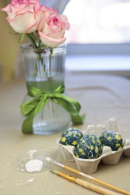 Paskalya için yumurta tepsisinde renkli yumurtalar var. Sarı noktalı yeşil yumurtalar, beyaz noktalar ve çizgiler. Yakınlarda fırçalar ve boyalar