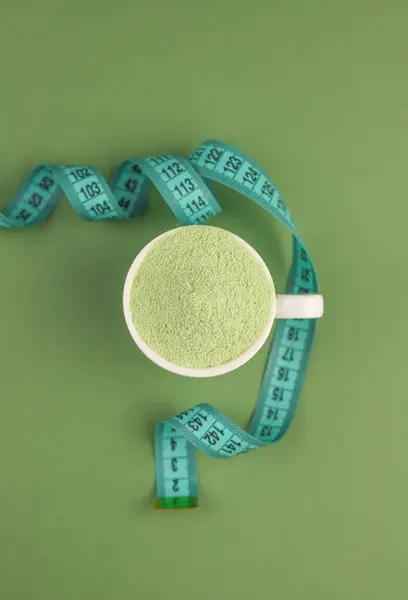 in a white cup there is a light green powder. next to a centimeter. healthy matcha tea. light green background