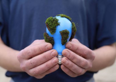 social problems. Earth Day. a blue light bulb with green moss is protected in the hands of a man clipart