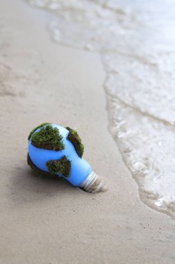 social problems. Earth Day. blue light bulb with green moss in the sand on the seashore clipart