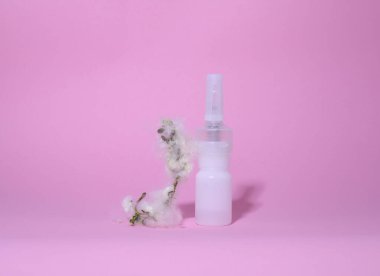 Alerji. Hastalık. Pembe bir arka planda beyaz bir şişe ilaç ve kabarık bir dal var.