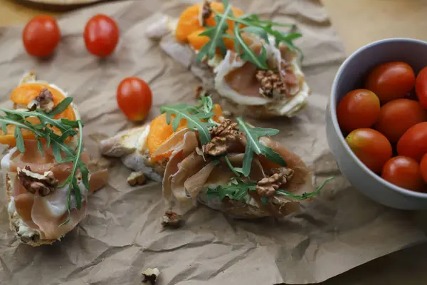 İtalyan aperatifi bruschetta. Ekmek, kayısı, peynir ve roka ile süslenmiş hazır bruschetta, ahşap bir masa ve parşömen üzerinde duruyor. Akşam yemeği için içki yakında.
