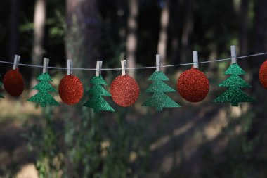 New Year's garland of green shiny fir trees and red shiny balls on clothespins in nature clipart