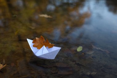 Suda, nehirde ya da gölde kağıt tekne. Teknede bir sonbahar yaprağı var. sonbahar