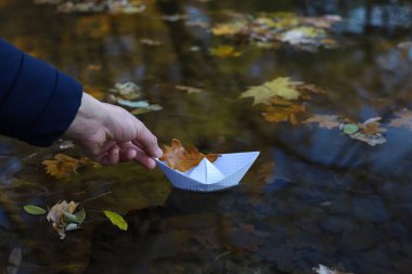 Bir el kağıt bir tekneyi suya, nehre ya da göle indirir. Teknede bir sonbahar yaprağı var. sonbahar