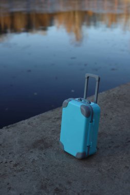Mavi bir valiz gölün arka planında kıyıda duruyor.