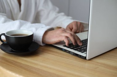 Tatilde ya da evde çevrimiçi iş. Beyaz dizüstü bilgisayarı olan beyaz önlüklü bir erkek. Onun yanında bir fincan kahve.