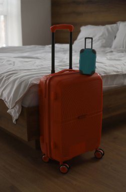 Turuncu büyük bir seyahat çantası ve beyaz çarşaflı bir yatağın arka planında küçük mavi bir bavul.