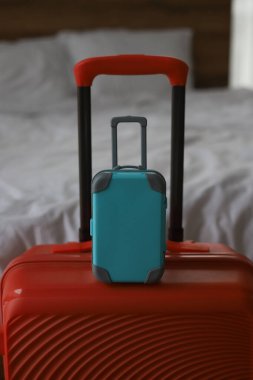 Turuncu büyük bir seyahat çantası ve beyaz çarşaflı bir yatağın arka planında küçük mavi bir bavul.