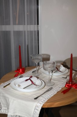 Romantik bir akşam yemeği için masayı hazırla. Beyaz masa örtüsü, tabaklar, temiz bardaklar ve bordo mumlar.
