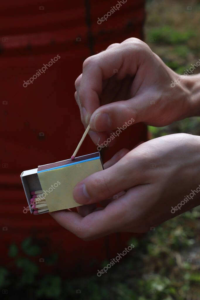 Matchbox with matches in a person's hands. in the background there is a red barrel