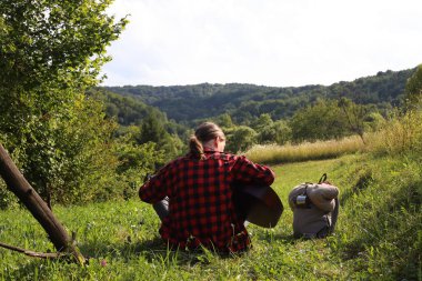 Doğada akustik gitarı olan kırmızı tişörtlü genç bir adam.