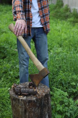Köyde çalış. Damalı turuncu gömlekli ve mavi eldivenli bir adam odun kesiyor.