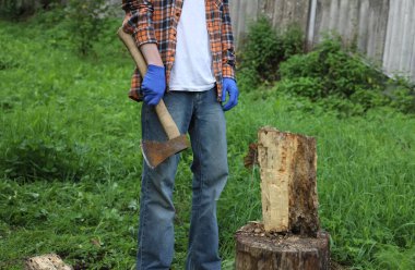 Köyde çalış. Damalı turuncu gömlekli ve mavi eldivenli bir adam odun kesiyor.