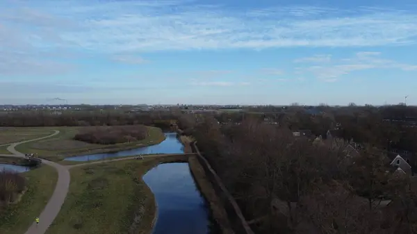 Parlak bulutlu bir gökyüzünün altında ağaçlarla çevrili güzel bir şehrin hava görüntüsü.