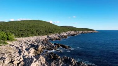 Arkaplanda dağlar olan okyanusa bakan bir uçurum çarpıcı bir su, gökyüzü, bulutlar ve uzak bir ufuk manzarası sunuyor.